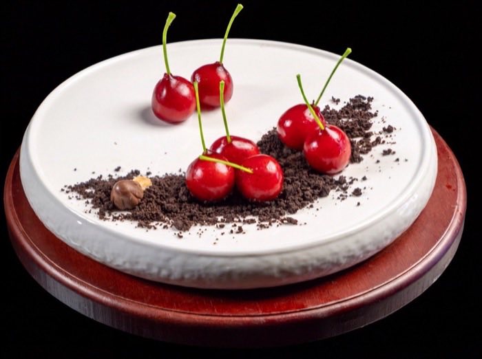 Fresh cherries arranged with dark crumb on a white porcelain plate