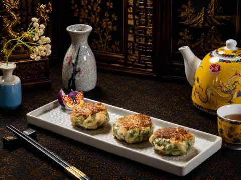 Three pan-fried chive cakes arranged on a long white plate