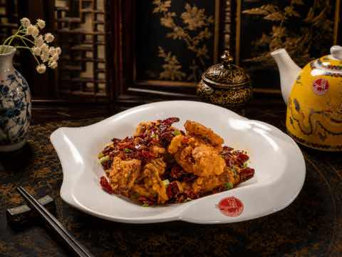 Crisp fried chicken pieces with dried chilies on a curved white plate