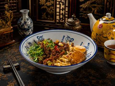 Noodle bowl with cumin beef, greens and a wedge of omelette