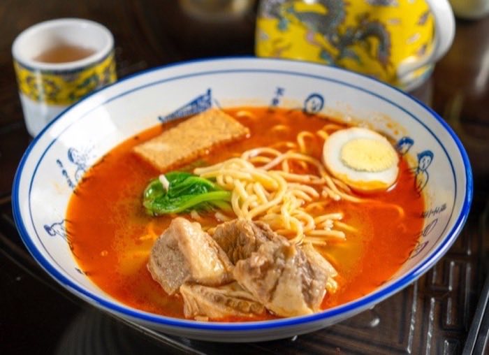 Noodle soup with fried tofu, egg and greens in a red broth