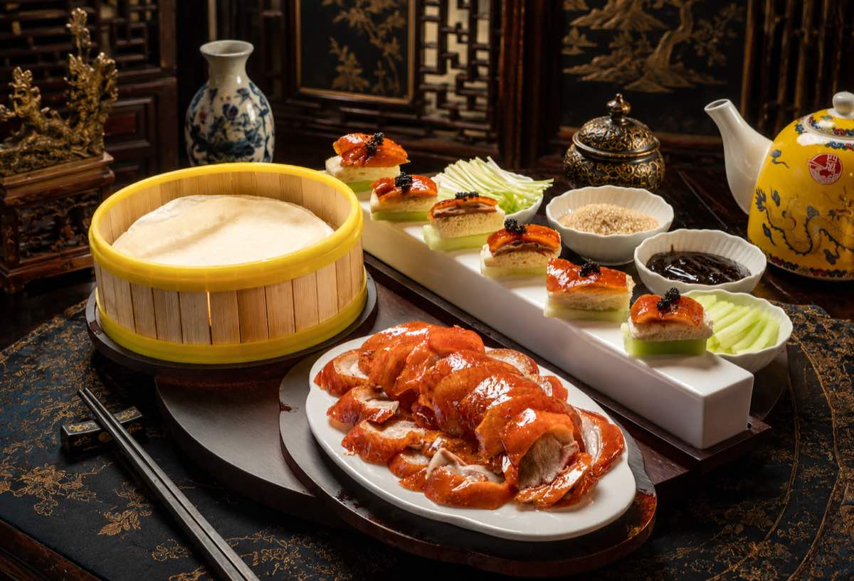 Peking duck carved into glossy slices, served with warm pancakes in a bamboo steamer, cucumber, spring onion and sweet bean sauce