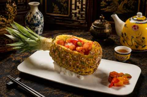 Fried rice served in a hollowed pineapple half on a white plate