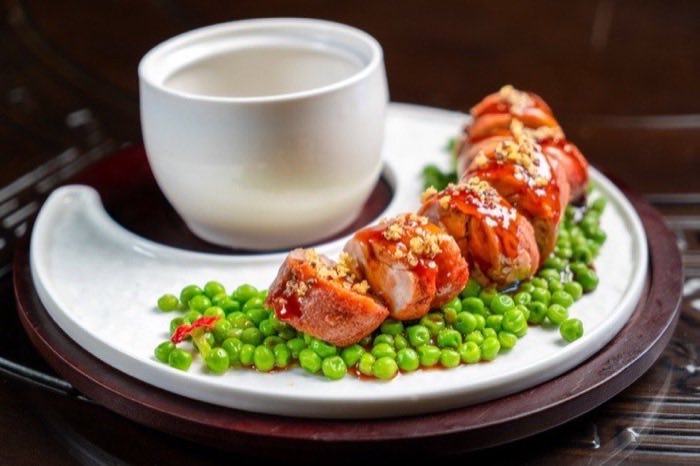 Neatly rolled morsels plated with garden peas beside a porcelain cup