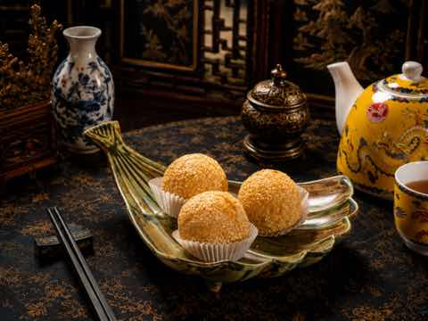 Sesame-coated fried dough balls served on a leaf-shaped dish