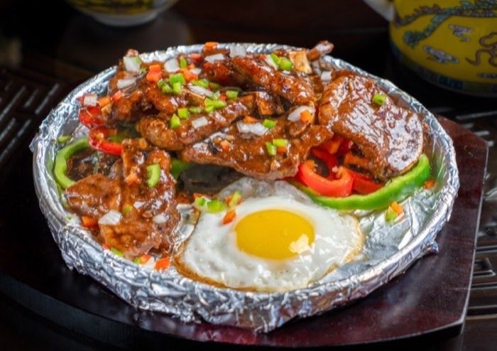 Sizzling beef with peppers and a fried egg on a foil-lined plate