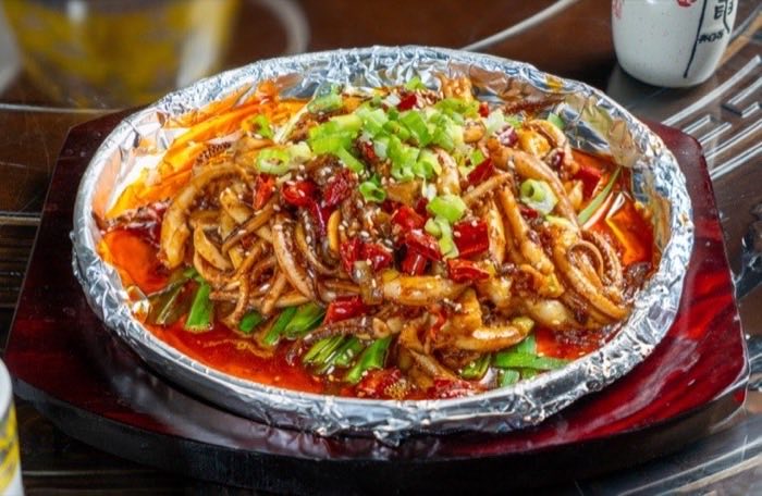 Squid served sizzling on a foil-lined hot plate with chili and greens