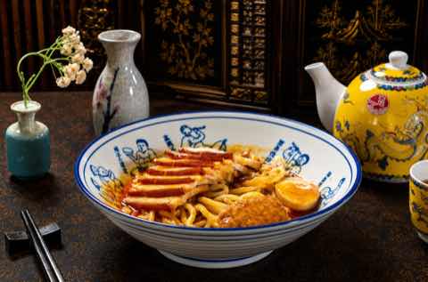 Noodle bowl fanned with sliced pork and a wedge of omelette
