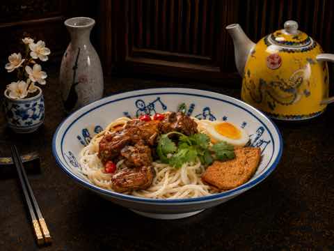 Spicy noodle bowl topped with braised meat, cilantro and egg