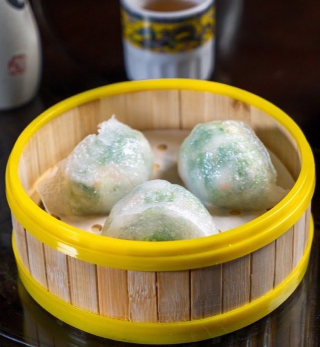 Translucent steamed dumplings with green filling in a bamboo basket