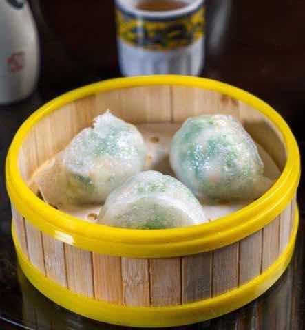 Translucent steamed dumplings with green filling in a bamboo basket